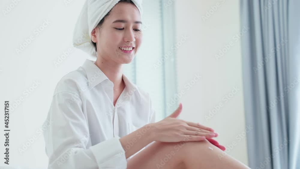 Asian beautiful woman put smooth and soft skin care on legs in bedroom