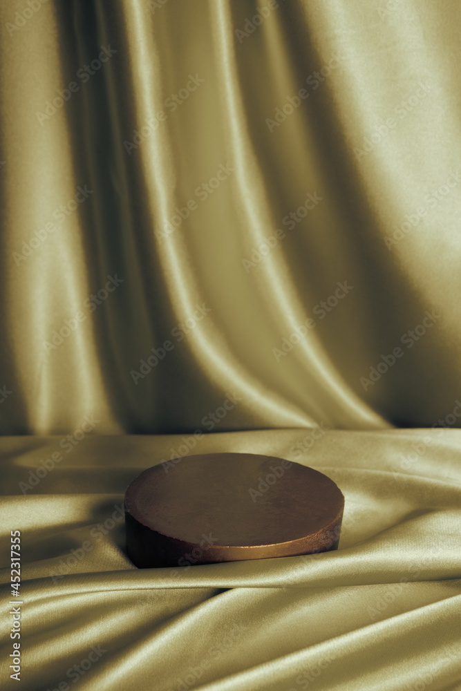 Empty podium or pedestal for perfume or cosmetic product on golden satin fabric with folds