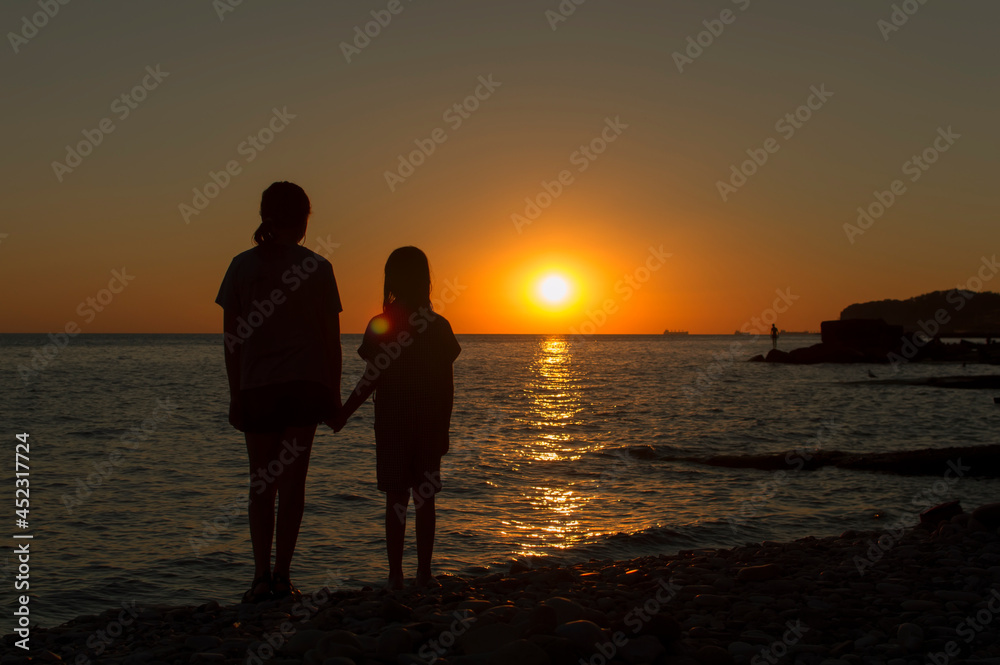Silhouettes of children against the sunset on the seashore. The concept of family values.