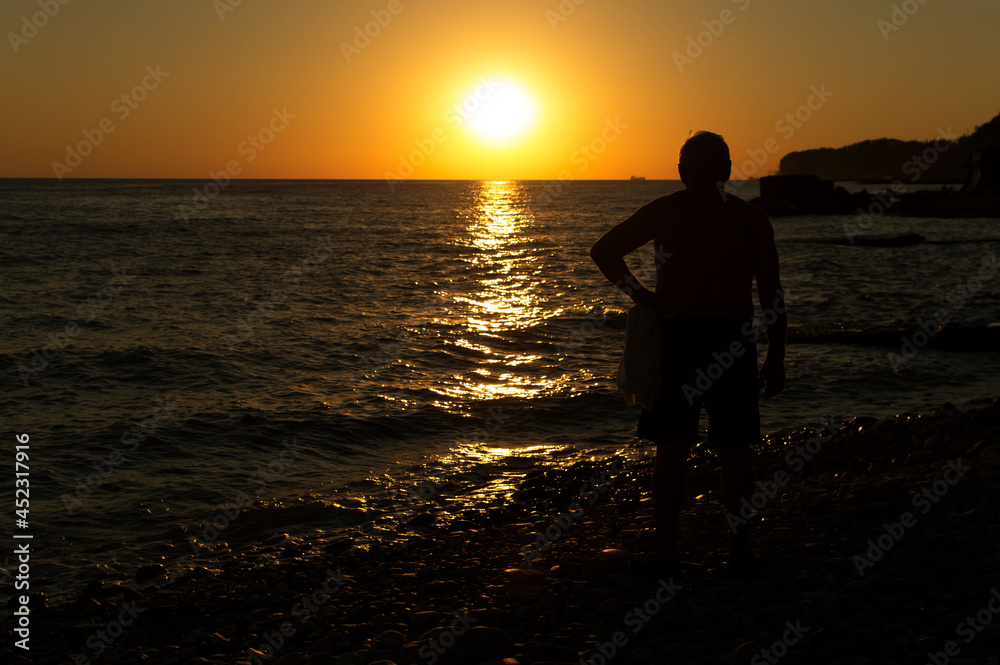 The silhouette of a man against the background of a sunset on the seashore. Loneliness.