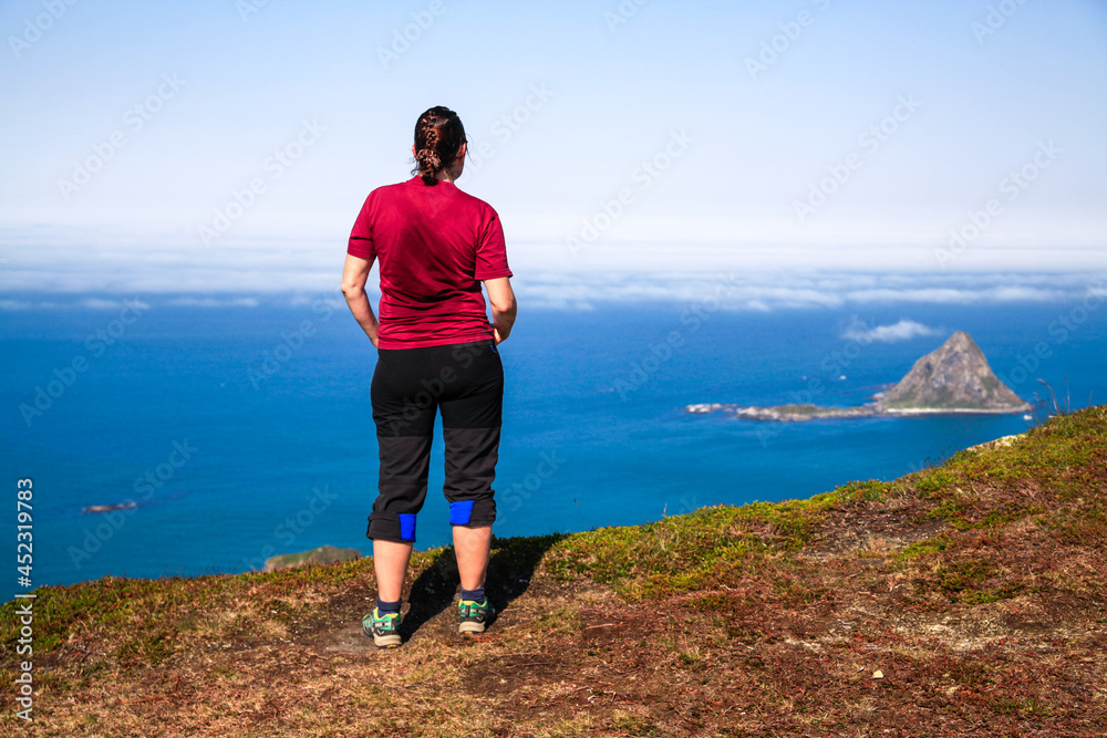 Woman climber rests on mountain top and looks at sunny air panorama of ocean
