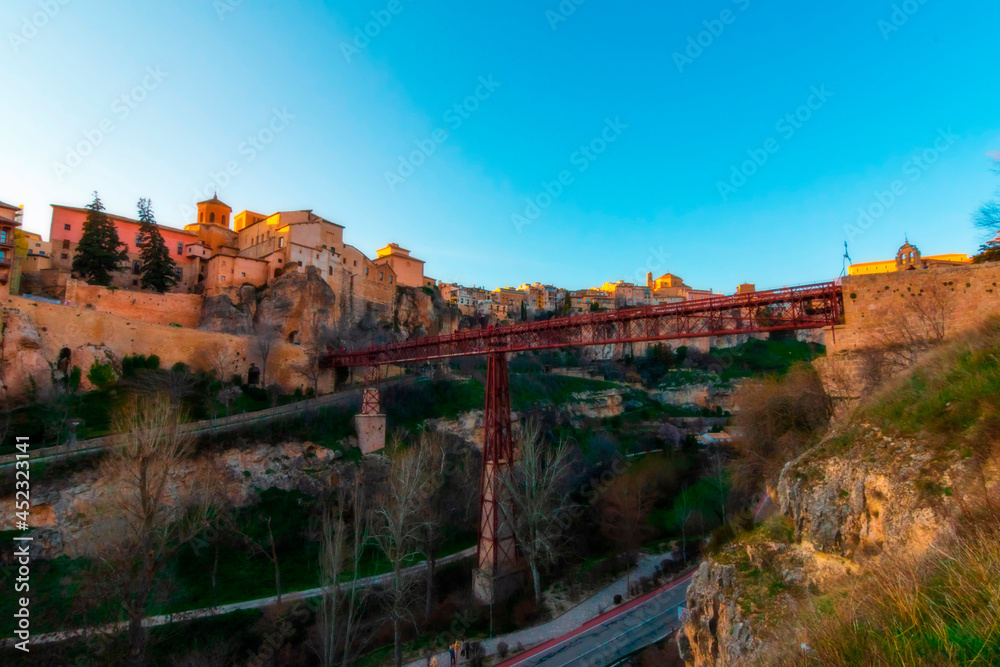 Cityscape in old town changing light at sunset; Hanging houses with old town hanging over mountain and red bridge of San Pablo de Cuenca, world heritage site, Spain. Horizontal view