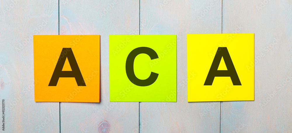 Three colored stickers with the text ACA on a light blue wooden background