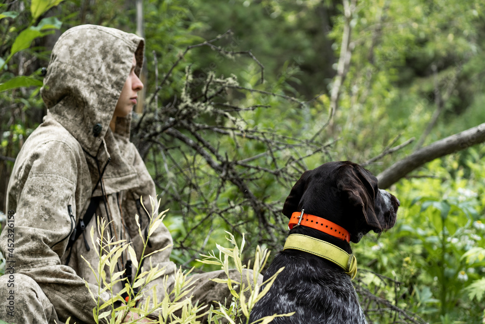 A girl hunter sits with her dog in the bushes. A girl hunts with a German drathaar