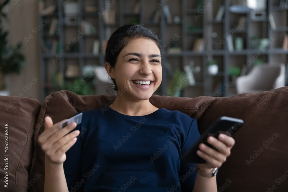Overjoyed Indian woman have fun shopping online on cellphone with credit debit card. Happy millennial mixed race female smile buying on internet using smartphone with secure bank system. Overjoyed Indian woman have fun shopping online on cellphone with credit debit card. Happy millennial mixed race female smile buying on internet using smartphone with secure bank system.