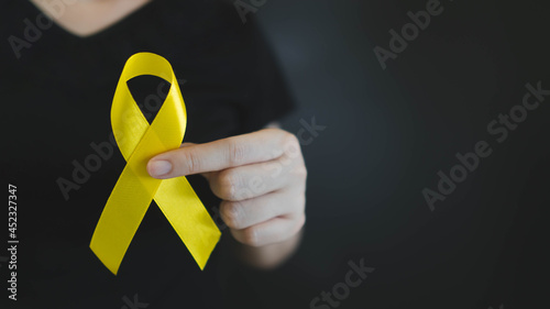 World suicide prevention day. Human hands holding yellow ribbon awareness symbol for preventing suicide on black background. Mental health care concept. photo