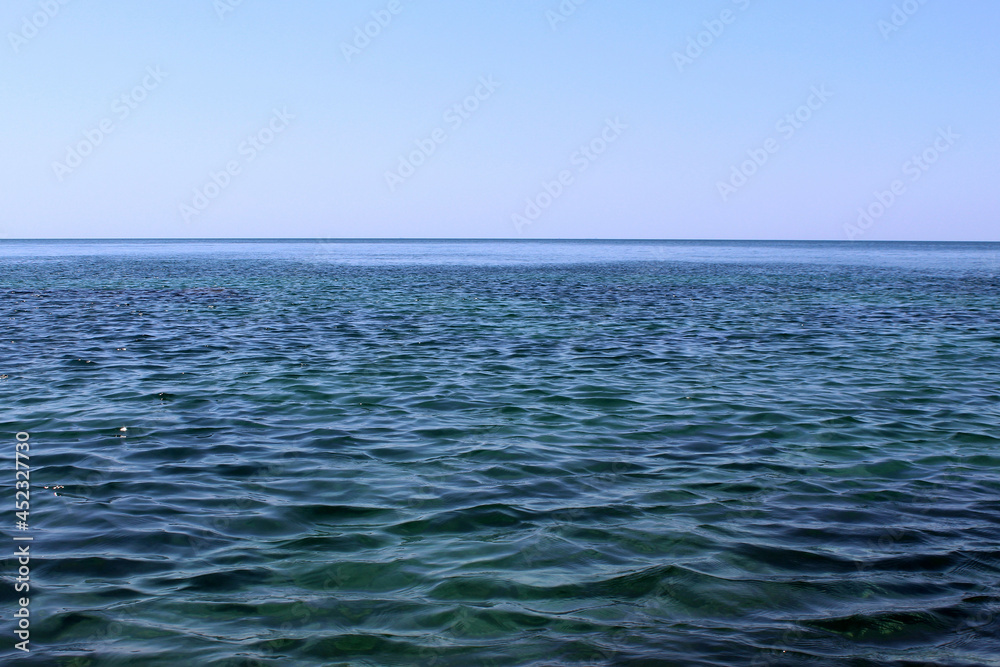 Obraz premium The calm sea stretches to the horizon with a cloudless sky.