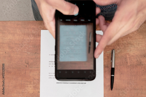 Cenital shot. Person photographing a contract with his smartphone. Detail shot