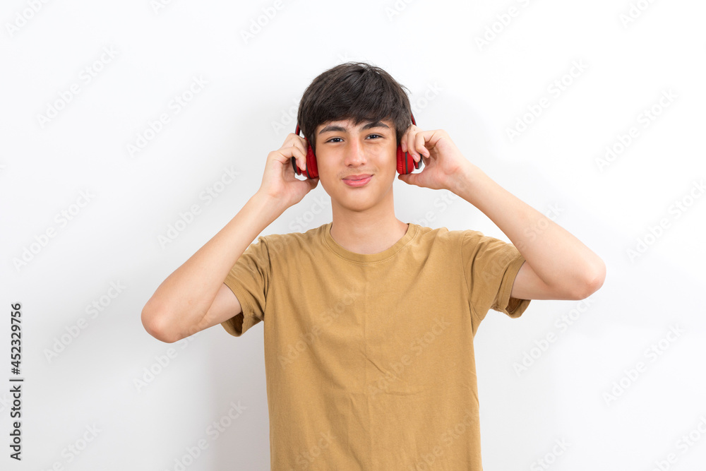 A teenager boy with wireless headphones on his head listens to music on a white background. A teenager boy with wireless headphones on his head listens to music on a white background.