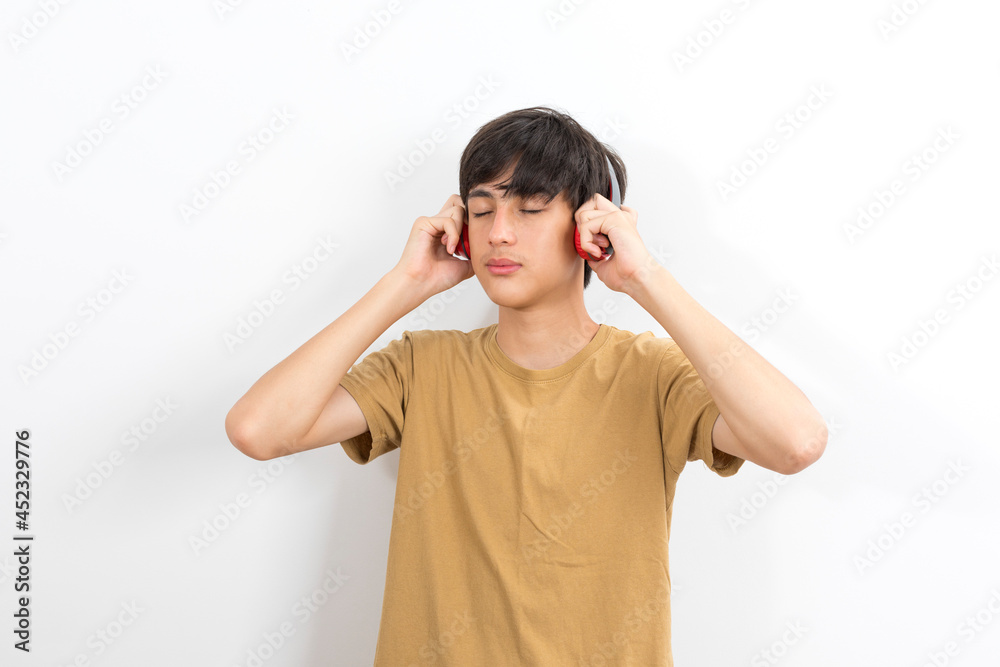 A teenager boy with wireless headphones on his head listens to music on a white background. A teenager boy with wireless headphones on his head listens to music on a white background.