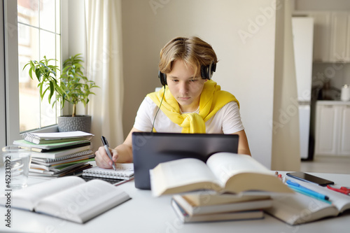 Teenager boy study at home. Online education and distance learning for children. School boy doing his physics homework using gadgets. Lessons on the internet for high school students