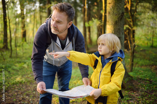 Schoolchild and his mature father hiking together and exploring nature. Little boy with dad looking map during orienteering in forest. Adventure, scouting and hiking tourism for kids. photo