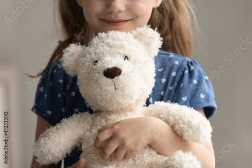 Close up of teddy bear in arms of child. Happy smiling little girl kid holding, hugging toy, playing with plush soft friend. Cropped portrait. Childhood, preschooler, playtime, childcare concept © fizkes