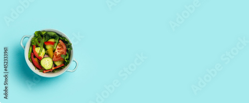Vegetable salad in a blue bowl on a light blue background. Top view, flat lay. Banner