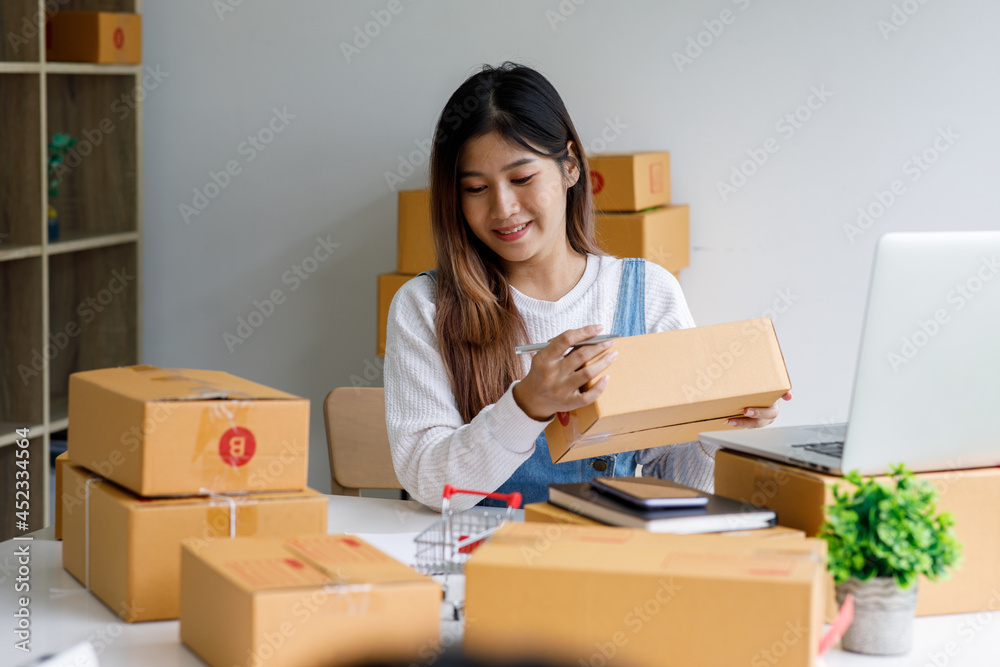 Portrait of Starting Small business entrepreneur SME freelance,Portrait young woman working at home office, BOX,smartphone,laptop, online, marketing, packaging, delivery, SME, e-commerce concept