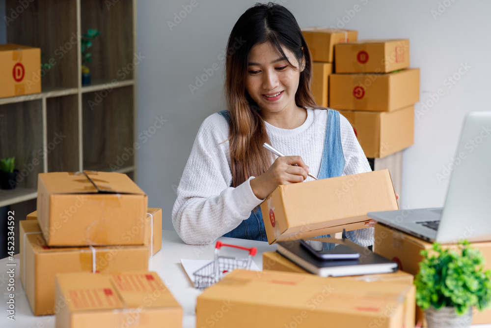 Portrait of Starting Small business entrepreneur SME freelance,Portrait young woman working at home office, BOX,smartphone,laptop, online, marketing, packaging, delivery, SME, e-commerce concept Portrait of Starting Small business entrepreneur SME freelance,Portrait young woman working at home office, BOX,smartphone,laptop, online, marketing, packaging, delivery, SME, e-commerce concept