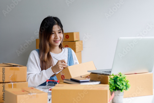 Portrait of Starting Small business entrepreneur SME freelance,Portrait young woman working at home office, BOX,smartphone,laptop, online, marketing, packaging, delivery, SME, e-commerce concept