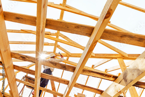 Construction of a wooden roof. The constructed structure of beams and partitions against the background of the builder fixing the details of the structure. Foreground. Selective focus © Dmitry