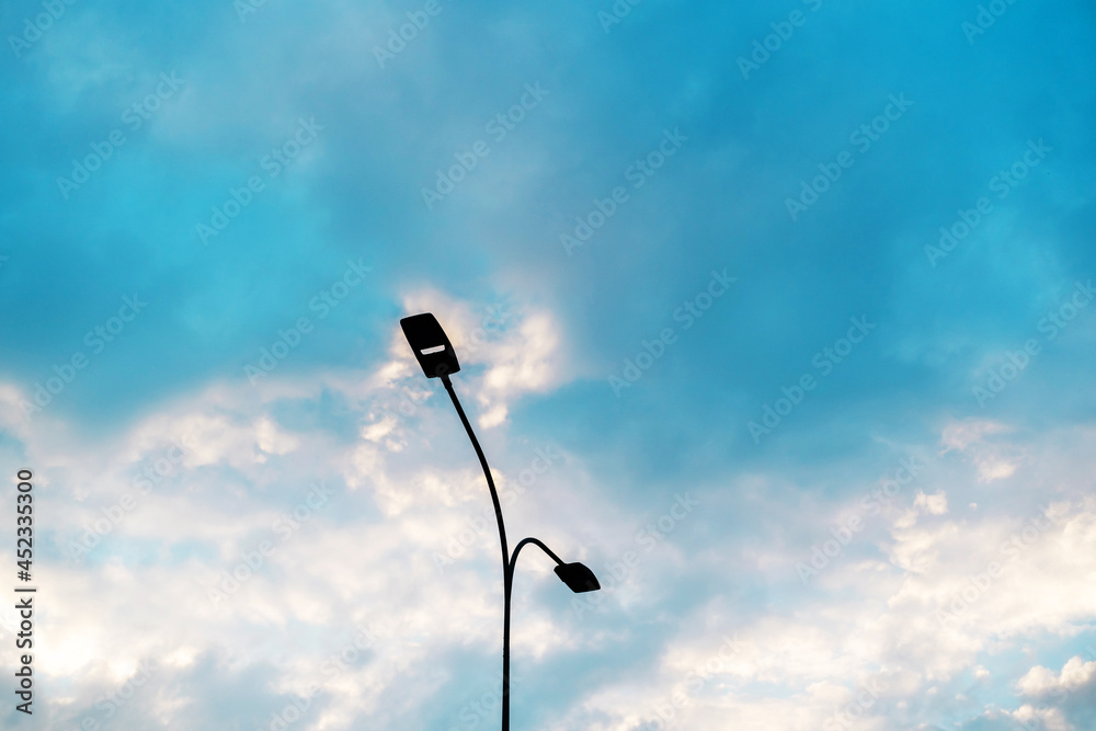 Lamp post against the background of the cloudy sky. Urban street lighting system with double lamps. Copy space