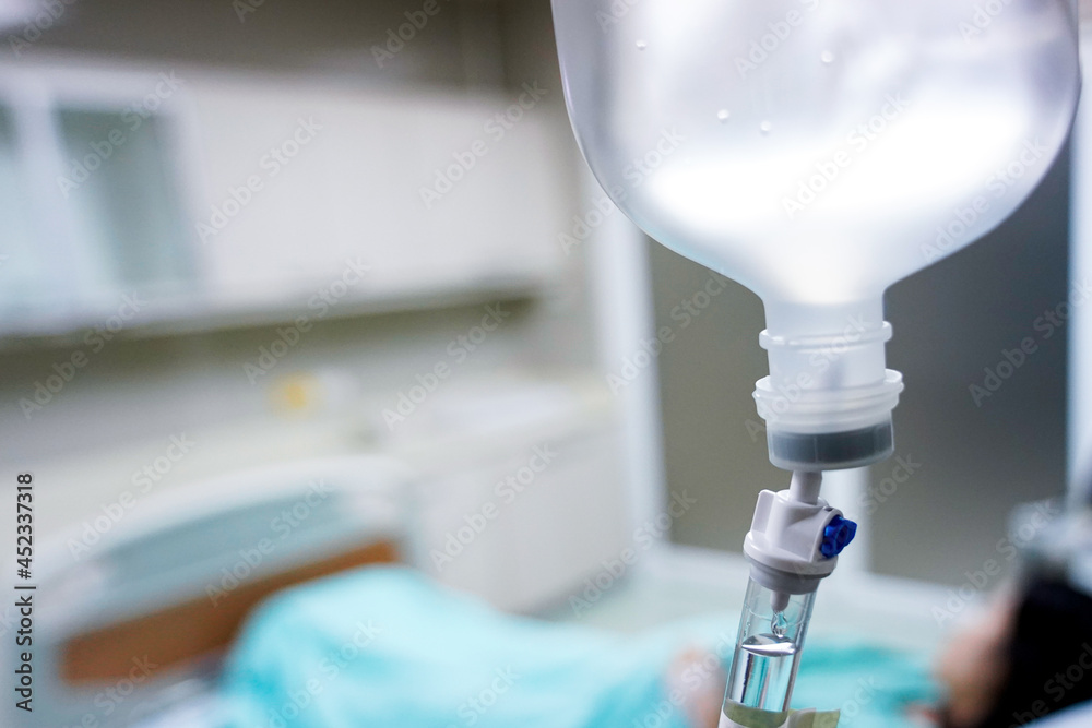 Close up Infusion bottle pump with saline solution drip and clipping path for patient admit room in hospital. Patient is waiting for doctor on bed preparing for surgery or diagnose in green dress. Close up Infusion bottle pump with saline solution drip and clipping path for patient admit room in hospital. Patient is waiting for doctor on bed preparing for surgery or diagnose in green dress.
