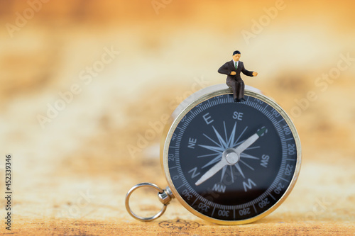 Miniature Business man people office worker sitting on golden compass thinking business plan solve problem using for Accounting Financial Banking business growth development and Commerce Strategy Plan