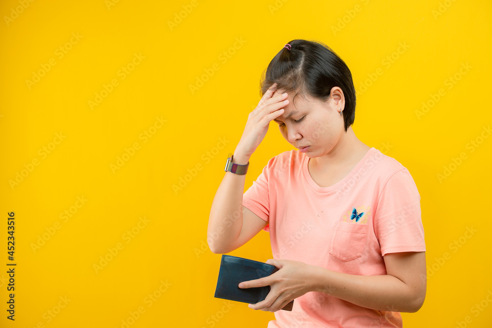 Portrait of a woman holding a wallet regretting that there is no money in her purse against a yellow background.concept saving. Portrait of a woman holding a wallet regretting that there is no money in her purse against a yellow background.concept saving.