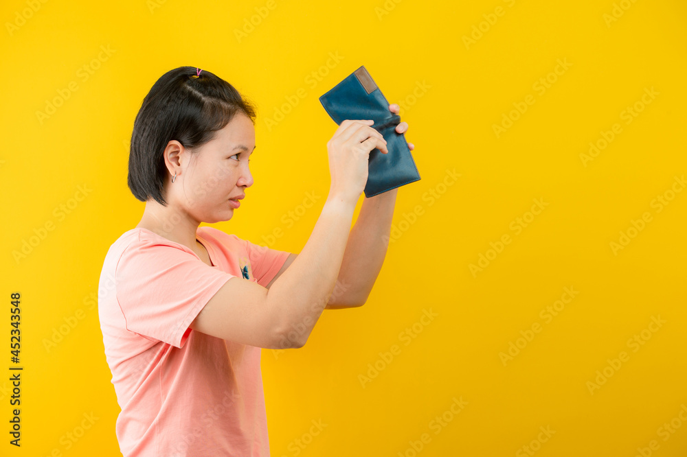 Portrait of a woman holding a wallet regretting that there is no money in her purse against a yellow background.concept saving. Portrait of a woman holding a wallet regretting that there is no money in her purse against a yellow background.concept saving.