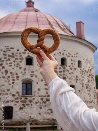 Vyborg pretzel in hand against the background of the old round tower (Symbol of Vyborg)