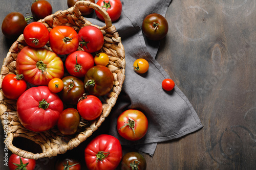 Fresh colorful ripe fall or summer heirloom variety tomatoes in a basket over dark wooden table background. Autumn and harvest concept.