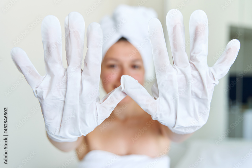 After a shower, a girl wrapped in a towel uses cosmetic gloves to