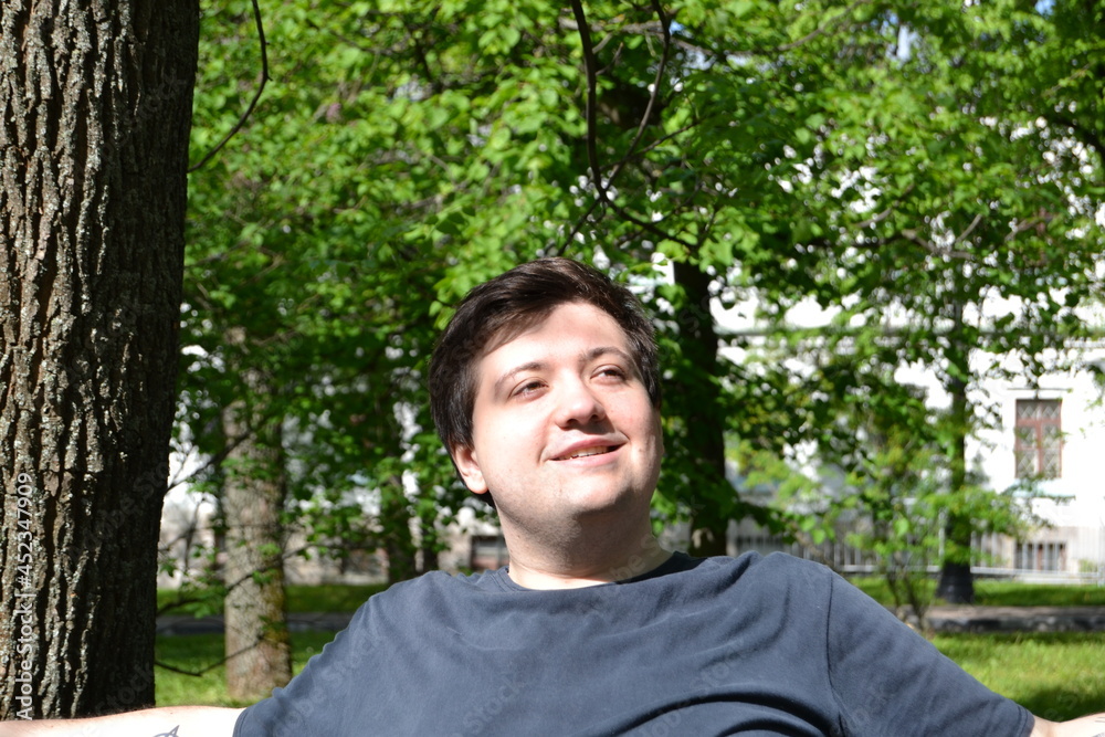 a young guy is resting in the park in a great mood, smiling a young guy is resting in the park in a great mood, smiling