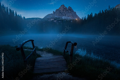 lago antorno di notte, con nebbia che si alza dal lago, e la luce del rifugio auronzo sotto le tre cime di lavaredo photo