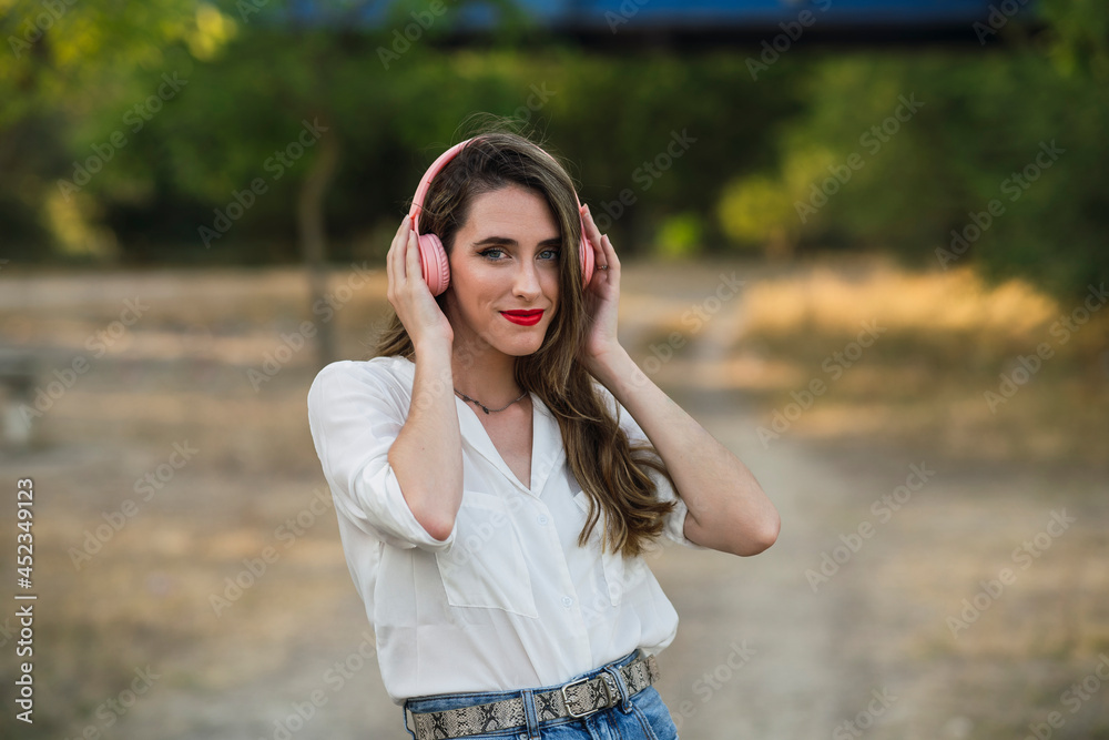 Chica joven al atardecer en un parque natural con smartphone y cascos