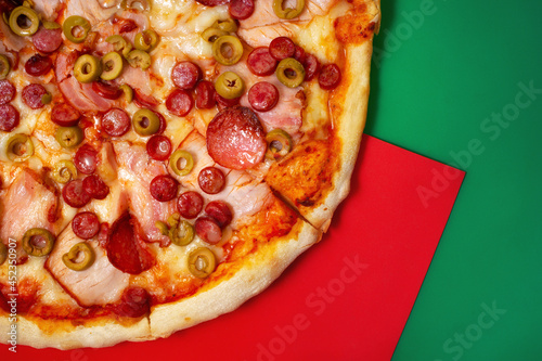 Italian pizza with ham and smoked sausages on red and green background with copy space area