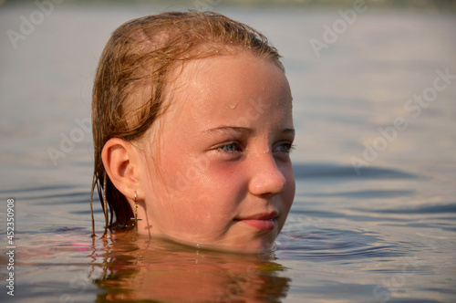 young beautiful girl relaxes in the water and admires the setting sun, close-up photo