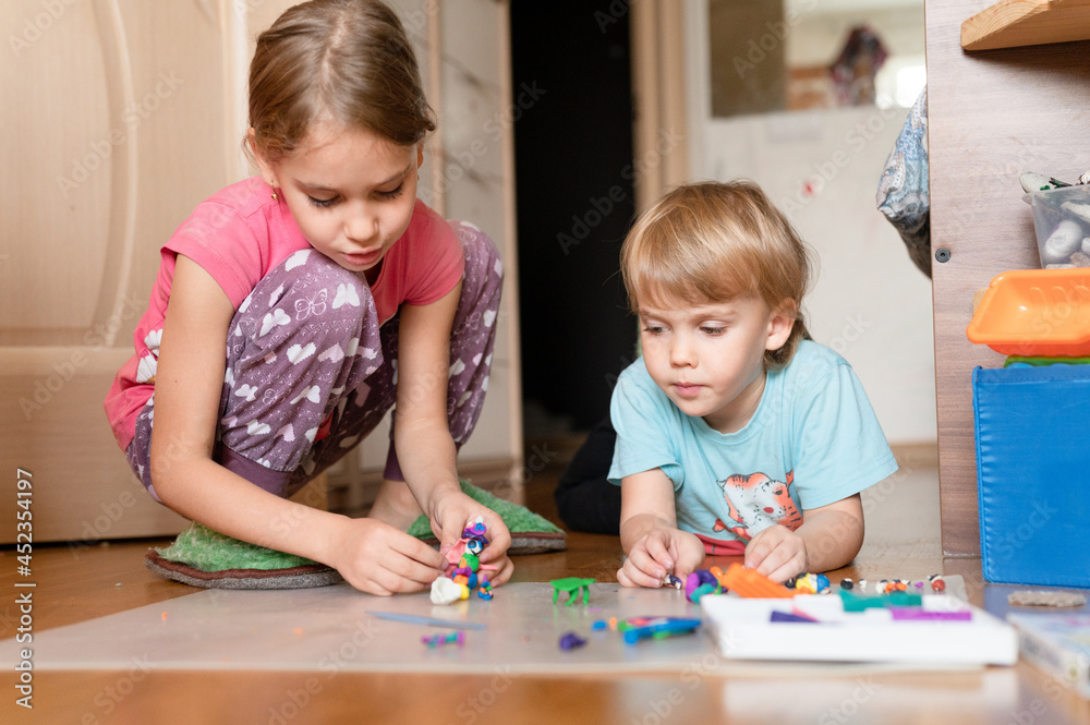 Russia, Moscow, October 2020 - two little happy kids a boy of four year old and a girl of seven year old siblings or friends at home on floor together playing and sculpting with plasticine Russia, Moscow, October 2020 - two little happy kids a boy of four year old and a girl of seven year old siblings or friends at home on floor together playing and sculpting with plasticine