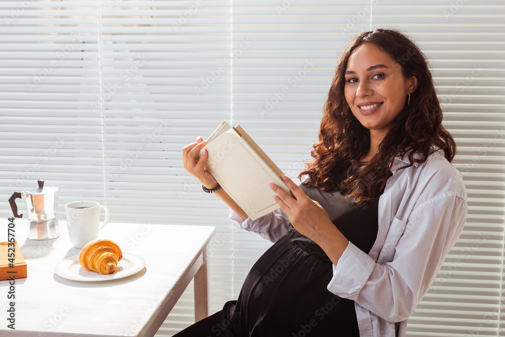 Pregnant woman eating and reading book at home. Morning, breakfast and pregnancy concept Pregnant woman eating and reading book at home. Morning, breakfast and pregnancy concept