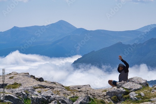 A young boy greets sitting in front of a high mountain landscape.