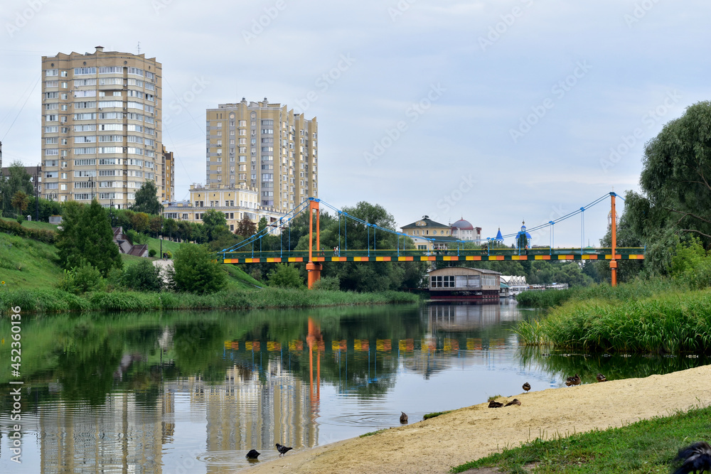 Two high-rise buildings are reflected on the surface of the river on the bank that they stand on.
