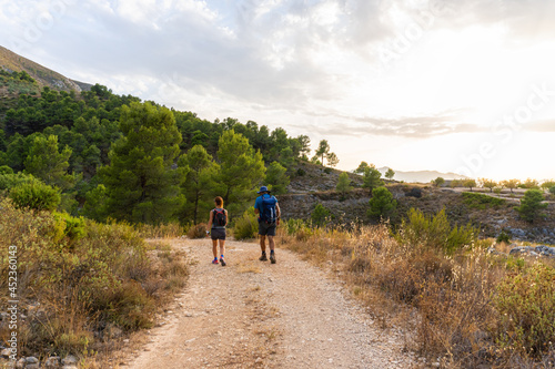 Woman and man hikers equipped with backpacks  walking along a dirt track  surrounded by nature  on a sunny afternoon.