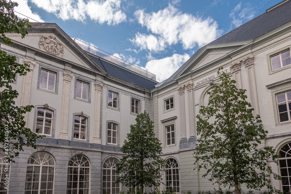 Fototapeta premium Gent, Flanders, Belgium - July 30, 2021: White palacial buidling and courtyard of Art Academy under blue cloudscape with some green foliage.