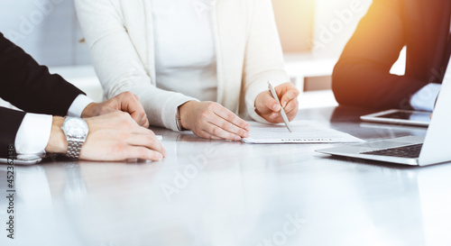 Business people discussing contract while working together in sunny modern office. Unknown businessman and woman with colleagues or lawyers at meeting