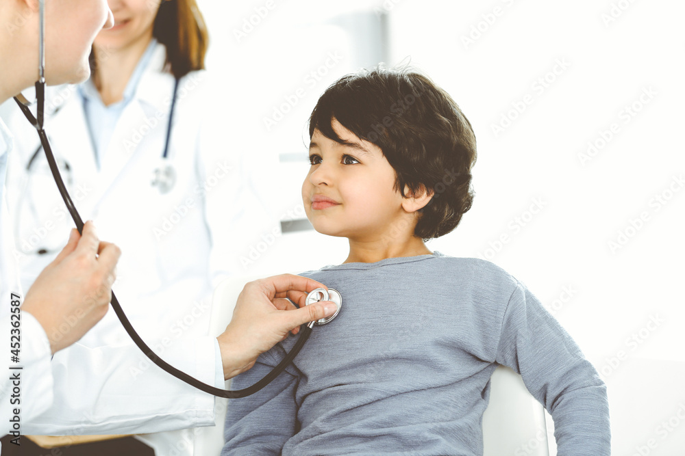 Doctor-woman examining a child patient by stethoscope. Cute arab boy at physician appointment. Medicine concept Doctor-woman examining a child patient by stethoscope. Cute arab boy at physician appointment. Medicine concept