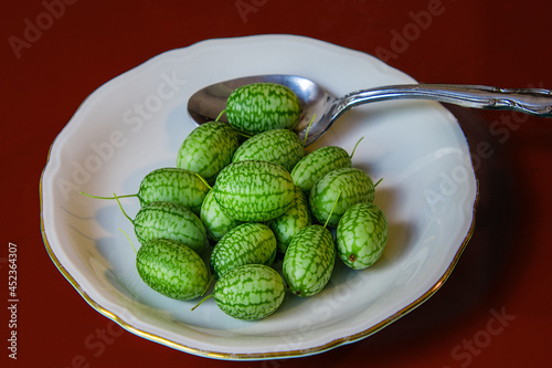 Fresh green cucamelon fruits in a dish with a spoon on a red table photo
