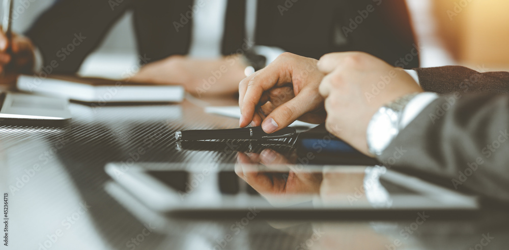 Unknown businessmen and woman sitting, working and discussing questions at meeting in sunny office, close-up. Success concept Unknown businessmen and woman sitting, working and discussing questions at meeting in sunny office, close-up. Success concept