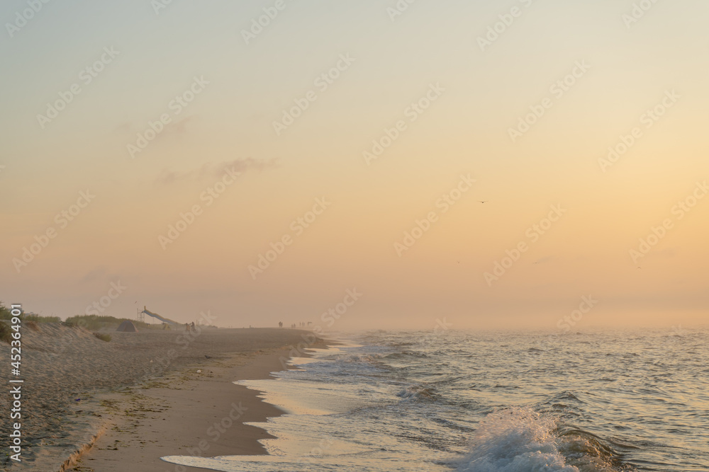 Foggy sunrise over the sea. Pastel shades. Beautiful landscape. Sandy beach of the ocean. Sunset sky. Clouds. Coast.