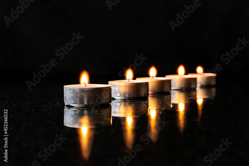 Five candles in a row on black reflected surface