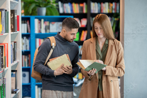 фотографія Two young students choosing books in college library or large bookshop