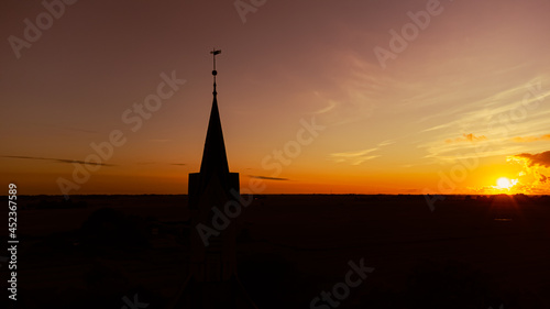 Kirche und Kirchturm im Sonnenuntergang mit weiter Landschaft und Natur im Hintergrund © Noah