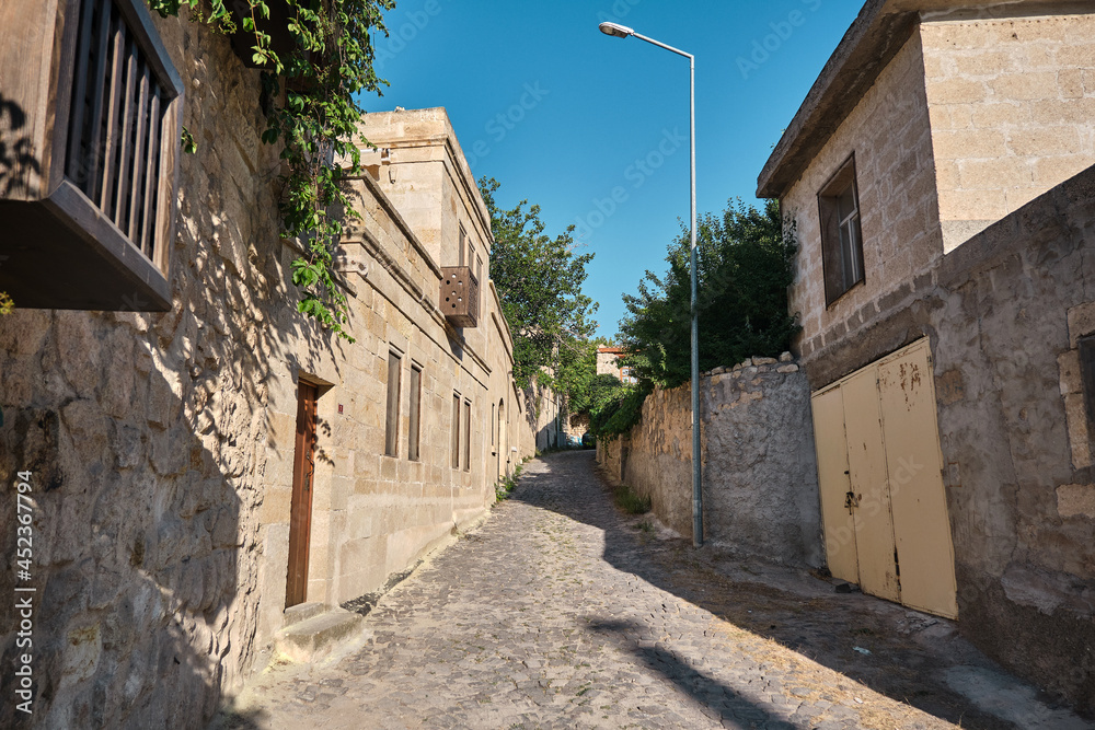 Narrow street in Urgup traditional houses made of limestone and cobblestone street and trees